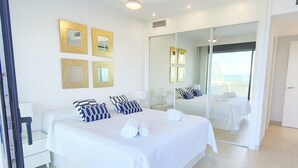 Een moderne hotelkamer met een groot bed, nachtkastjes, een spiegel en uitzicht op zee.