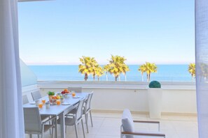 Ein Balkon mit Frühstückstisch, der Blick auf das klare, blaue Meer und Palmen bietet.
