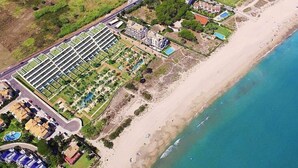 Luchtbeeld van een kusthotel met een lange rij kamers, een strand en een zwembad.