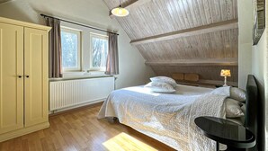 A bedroom with a bed, a nightstand, a wardrobe, a window with curtains, and a sloped ceiling. - Nice home in Rendeux with WiFi (Rendeux)