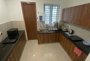 A kitchen with wooden cabinets, a microwave, a kettle, and a dish rack.