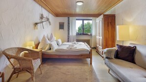 Une chambre avec un plafond en bois, un lit, une chaise en osier, un canapé et une fenêtre donnant sur un beau paysage.