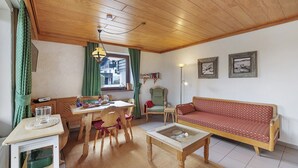 Un salon chaleureux avec un plafond en bois, un canapé, une table à manger avec des chaises et une lampe.
