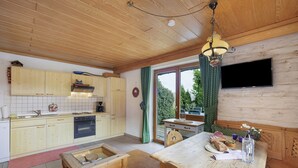 Un intérieur en bois comprenant une cuisine, un coin repas et un téléviseur fixé au mur.