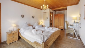 Un lit en bois avec du linge de lit blanc, une table de chevet avec une lampe, une armoire en bois et un bureau avec une chaise.
