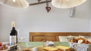 Une tête de lit en bois, une bouteille de vin, des verres, du fromage, du pain et un panier de bretzels sur une table.