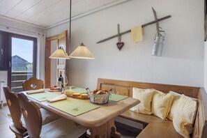 Ein Essbereich mit einem Holztisch, Stühlen, einer Bank, einer hängenden Leuchte und einem an der Wand befestigten Regal mit Herz-Dekoration und einem Metallbehälter.