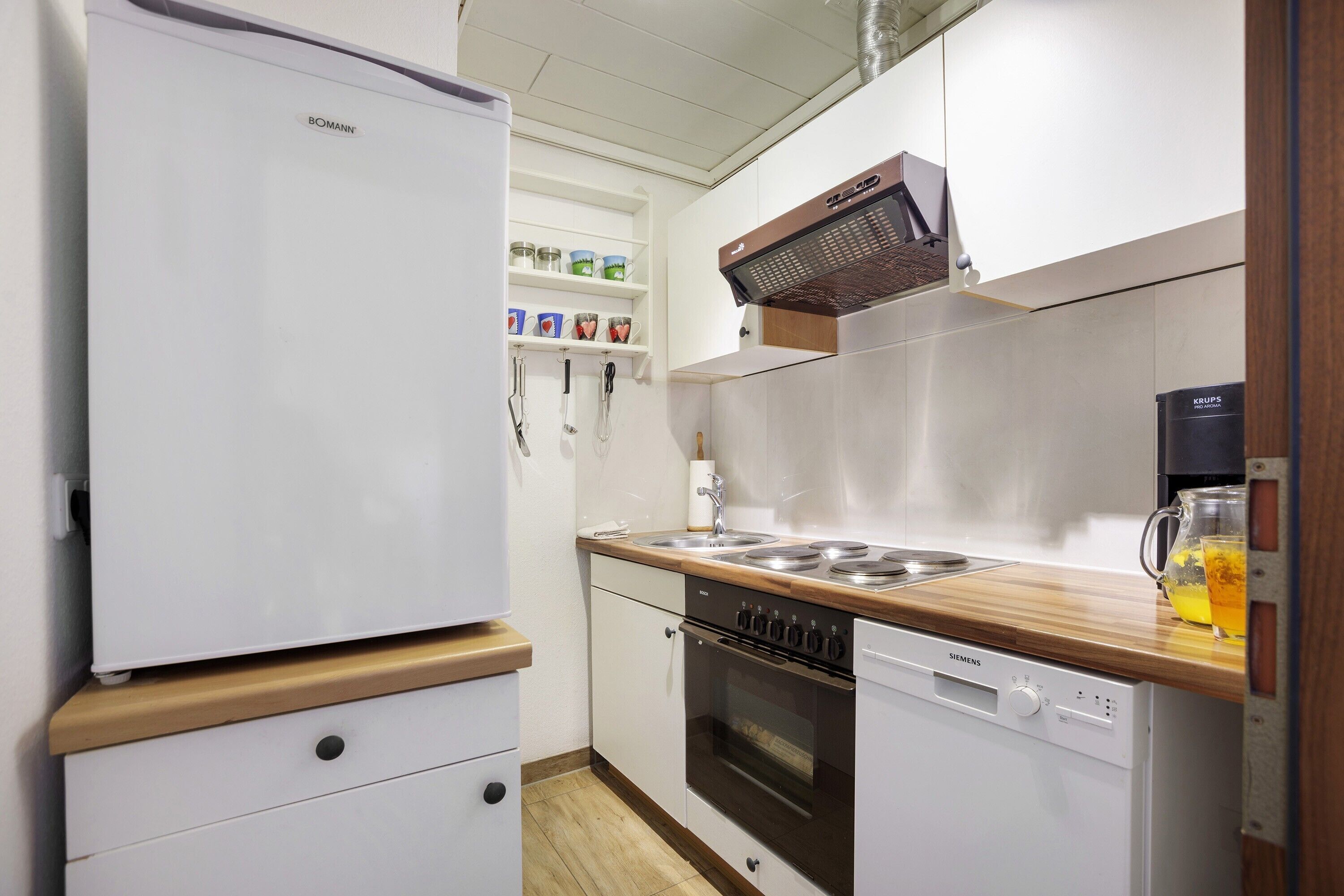 Una cocina con un refrigerador blanco, un lavavajillas Siemens, una encimera de madera y un horno Siemens.