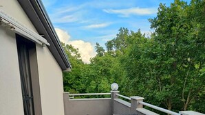 Ein Balkon mit Korbmöbeln und einem Glastisch, umgeben von einer Brüstung und Bäumen.
