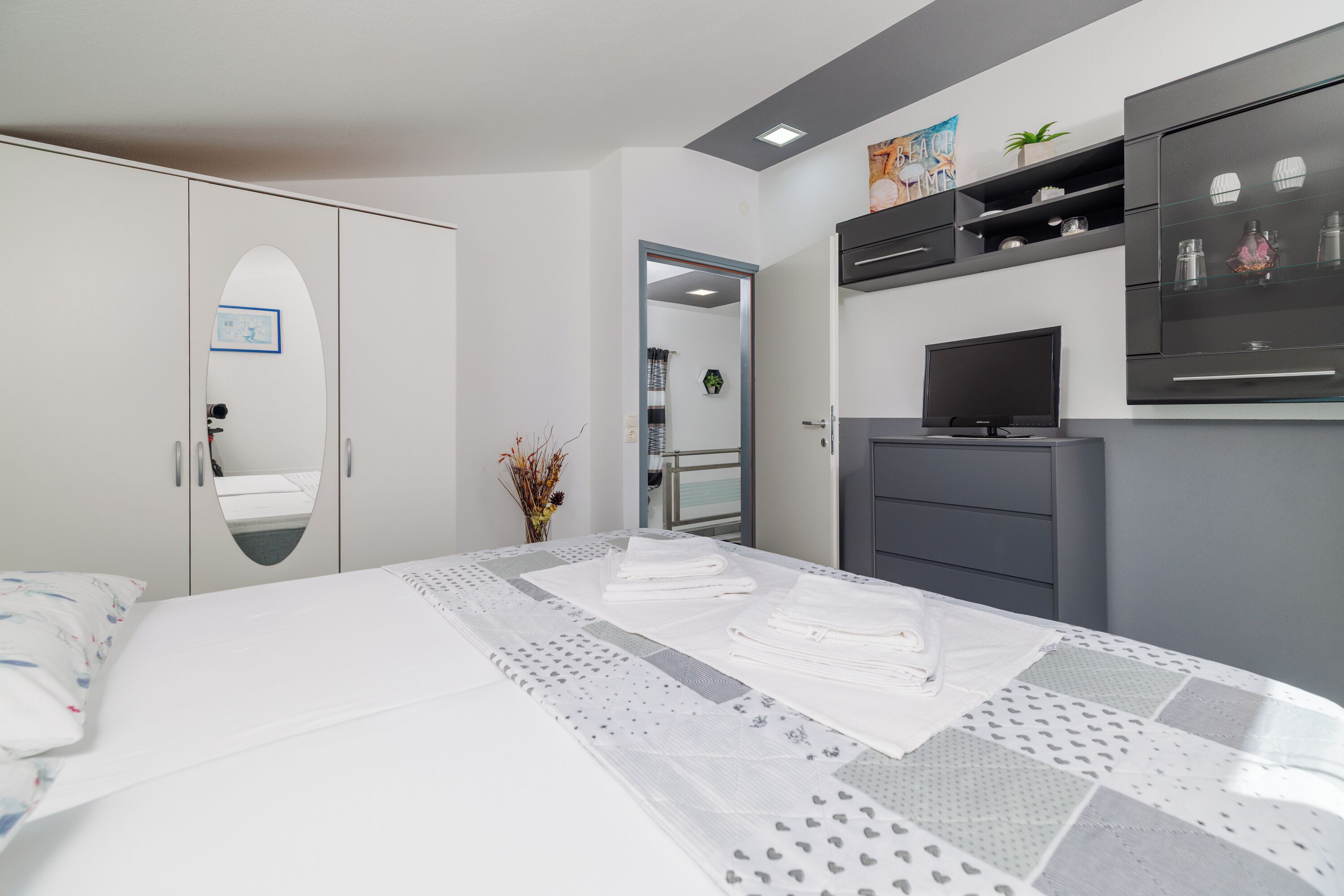 A bedroom with a bed, a wardrobe, a television, and a mirror.