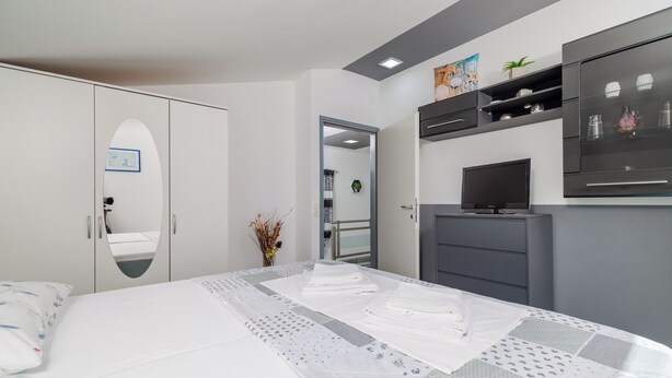 Ein Schlafzimmer mit Bett, Kleiderschrank, Fernseher und Spiegel.