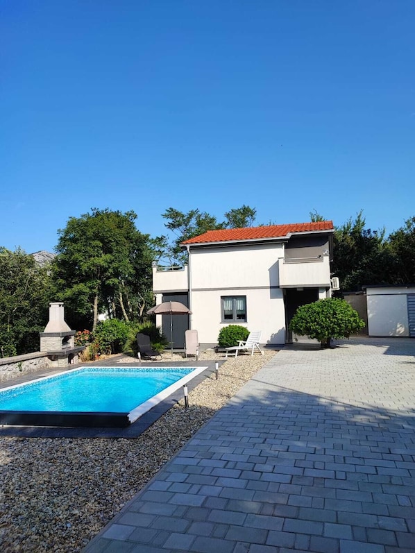 A modern two-story building with a swimming pool, outdoor seating, and a well-maintained garden.