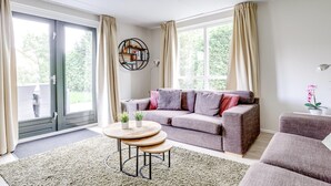 A modern living room with a grey sofa, a round wooden coffee table, and a large window with curtains. - Scenic Lakeview Cottage for 6 (Ewijk)