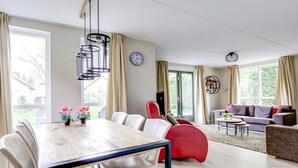 A modern living room with a dining area, large windows, and a red chair. - Scenic Lakeview Cottage for 6 (Ewijk)