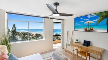 Ein Schlafzimmer mit großem Fenster, Deckenventilator, Schreibtisch und einem Gemälde mit Strandblick.
