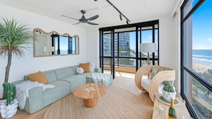 A modern living room with a sofa, coffee table, and a large window with a view of the city. - Pure Sunrise Oceanview 2BR Sub-Penthouse +Parking (Surfers Paradise)