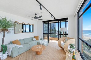 A modern living room with a sofa, coffee table, and a large window with a view of the city. - Pure Sunrise Oceanview 2BR Sub-Penthouse +Parking (Surfers Paradise)