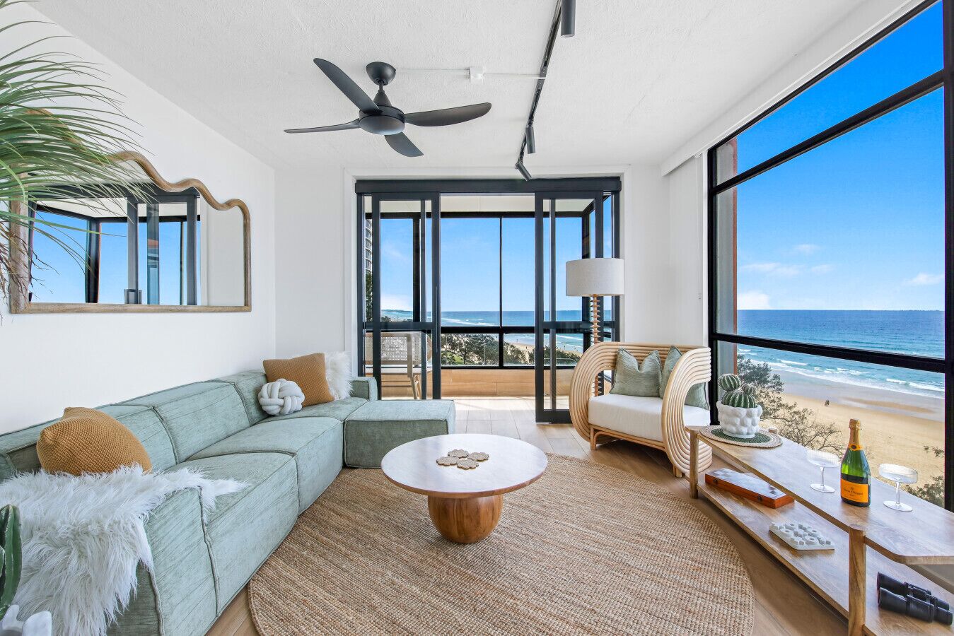 A spacious living room with a large window overlooking the beach, a ceiling fan, and a cozy seating area.