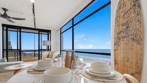 A dining area with a view of the beach, large windows, and a surfboard on the wall. - Pure Sunrise Oceanview 2BR Sub-Penthouse +Parking (Surfers Paradise)