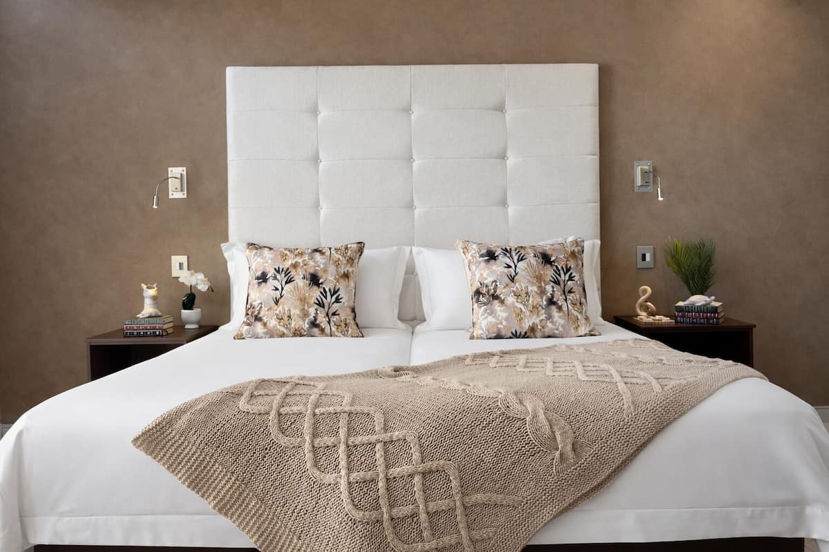 A bedroom with a tufted headboard, two decorative pillows, a woven throw blanket, and bedside tables with books and a small plant.