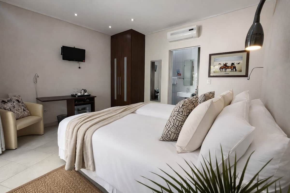 A bedroom with a bed, bedside table, chair, TV, wardrobe, mirror, and a plant.
