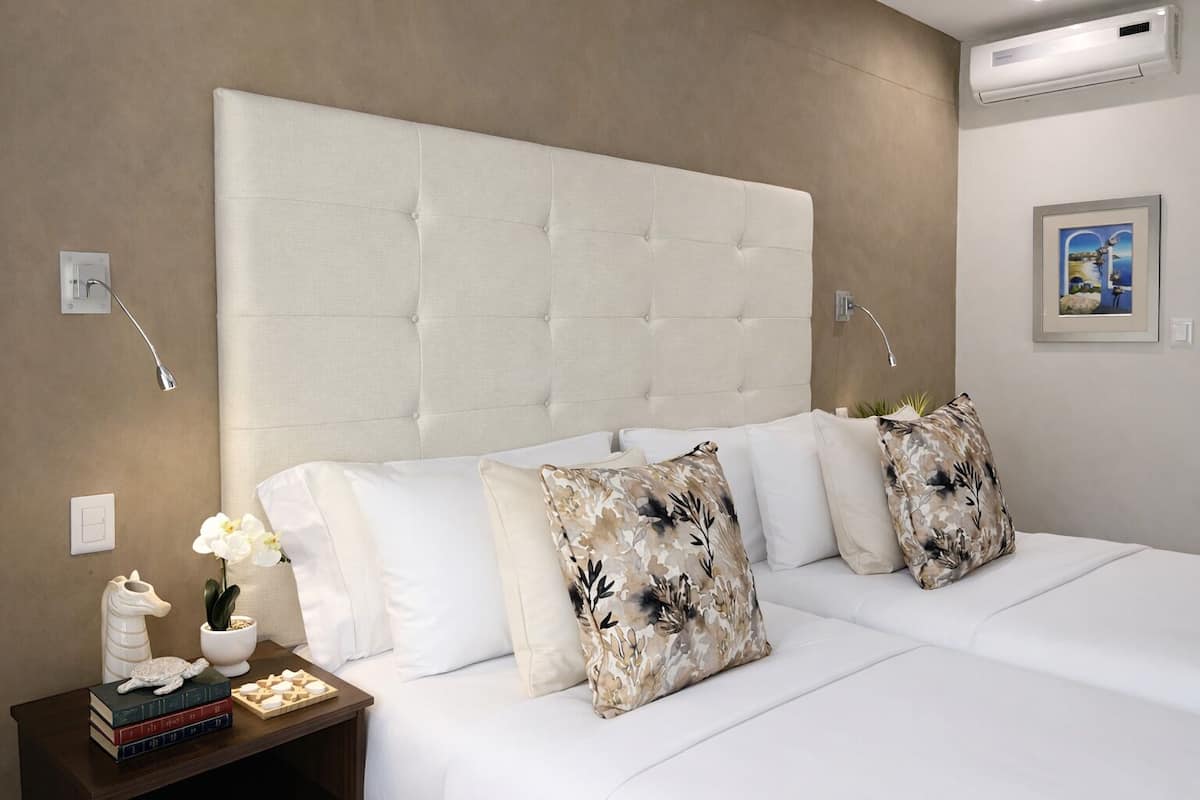 A hotel room with a large tufted headboard, white bedding, and decorative pillows.