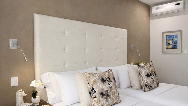 A hotel room with a large tufted headboard, white bedding, and decorative pillows. - Monte Bello Guesthouse (Windhoek)