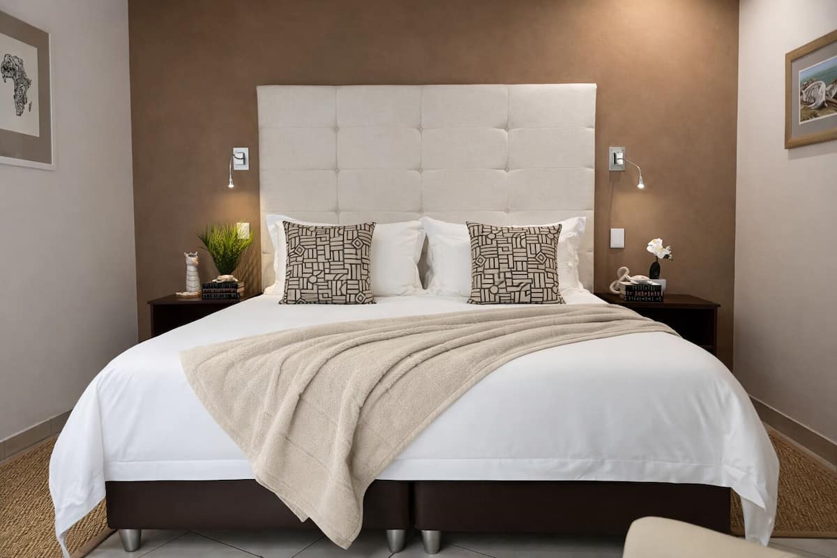 A neatly made bed with a tufted headboard, two patterned pillows, a beige throw blanket, and bedside tables with lamps and decorative items.