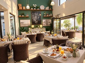 A restaurant with wicker furniture, breakfast spread, and artwork on the walls. - Monte Bello Guesthouse (Windhoek)