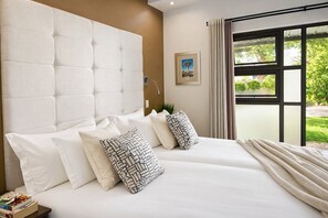A hotel room with a large bed, multiple pillows, a headboard, a window with curtains, and a framed picture on the wall. - Monte Bello Guesthouse (Windhoek)