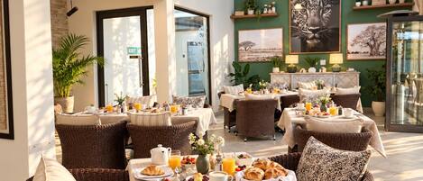 A breakfast setting with wicker furniture, tables with breakfast items, and a green wall with decorative items.