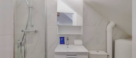 Un baño con ducha envuelta en vidrio, un lavabo blanco, un inodoro y un espejo sobre el lavabo.