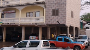 A multi-story building with a balcony, a garage, and parked vehicles. - BEL APPARTEMENT 1-Likouala! A stone's throw from downtown (LIBREVILLE)