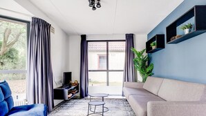 A modern living room with a sofa, a blue chair, a small table, and a TV.