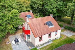 A two-story house with a red roof, solar panels, and a patio with chairs.