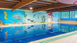 An indoor swimming pool with a mural of marine life, a blue bench, and a ceiling with exposed beams.