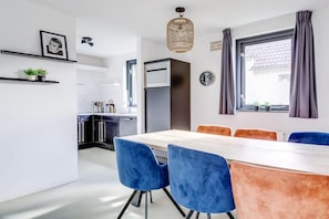 A modern kitchen with white cabinets, a built-in oven, and a dining area with a wooden table and blue chairs.
