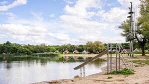 A lakeside area with a metal ladder leading into the water, surrounded by greenery and a few buildings in the background.