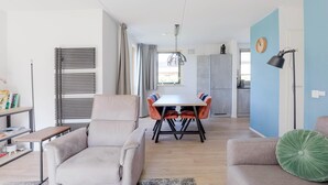 Moderni olohuone, jossa on sohva, ruokapöytä tuoleineen, keittiöalue ja sininen tehosteseinä.