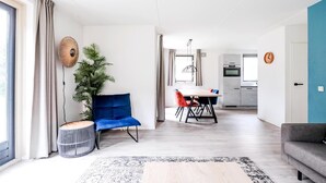 Uma sala de estar moderna com área de jantar, cozinha ao fundo e uma janela grande com cortinas.