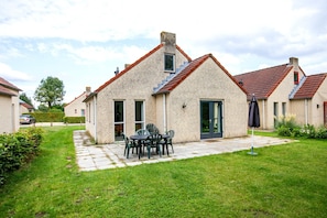 A brick house with a tiled roof, a patio with chairs, and a car parked in the driveway.
