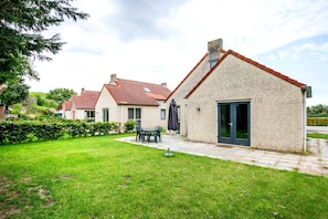 A residential area with brick houses, a grassy lawn, and a patio with outdoor furniture.
