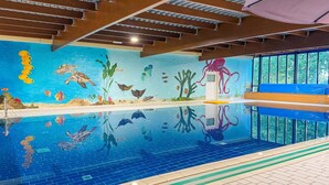 Piscina interna com um mural da vida marinha, prancha de salto e janela com vista para árvores.