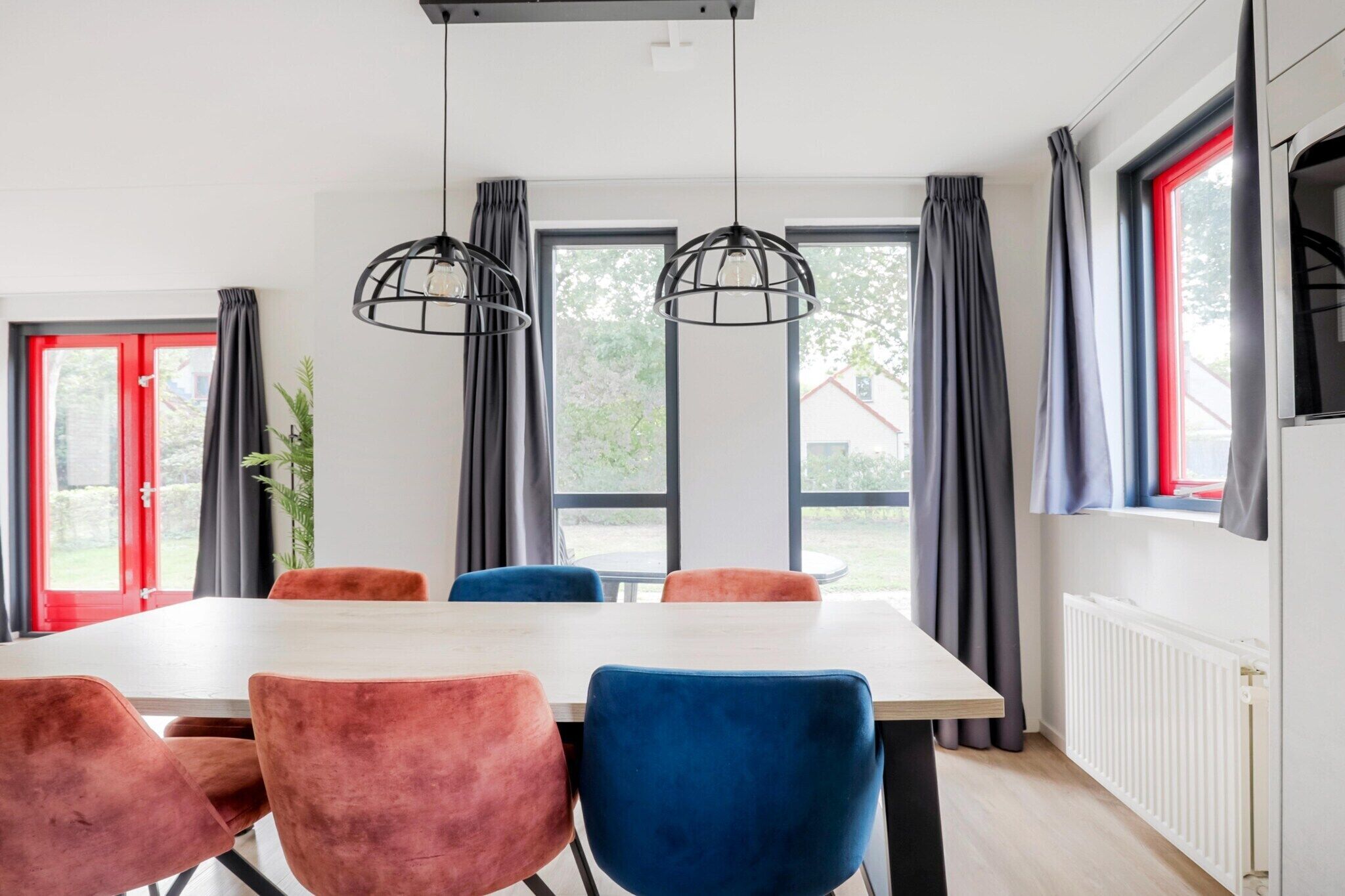 Zona pranzo con tavolo e sedie, ampie finestre con tende e lampadari a sospensione.