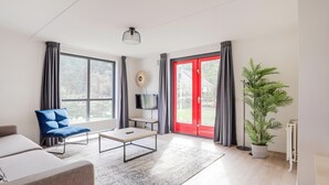 Uma sala de estar moderna com sofá, mesa de centro, televisão e uma grande janela com cortinas.