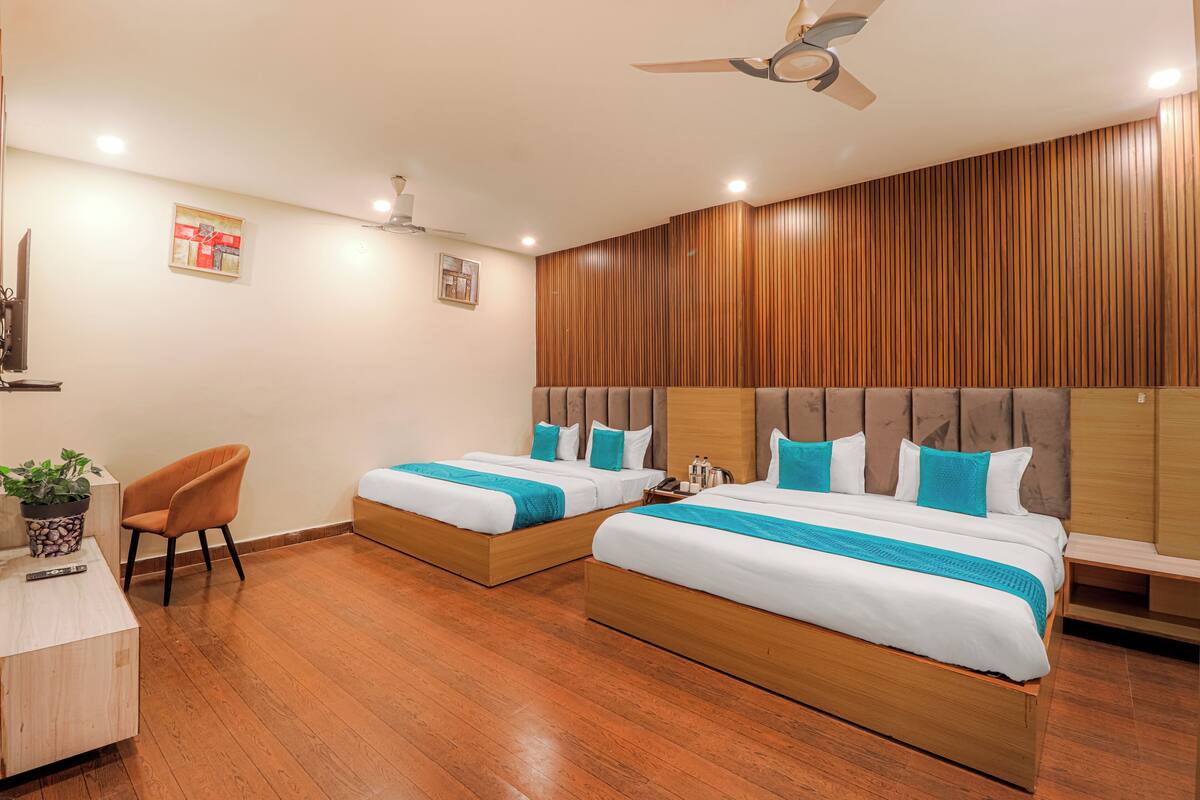 A hotel room with two beds, a desk, a chair, and a ceiling fan.