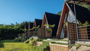 A row of modern, triangular-roofed cabins with a grassy yard and bamboo plants. - Royal VIP Glamping Kintamani (Kintamani)