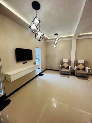 Ein modernes Wohnzimmer mit Flachbildfernseher, zwei Sofas und Pendelleuchten.