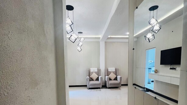 Un pasillo que conduce a una habitación con dos sillas, un televisor de pantalla plana montado en la pared y una lámpara moderna.