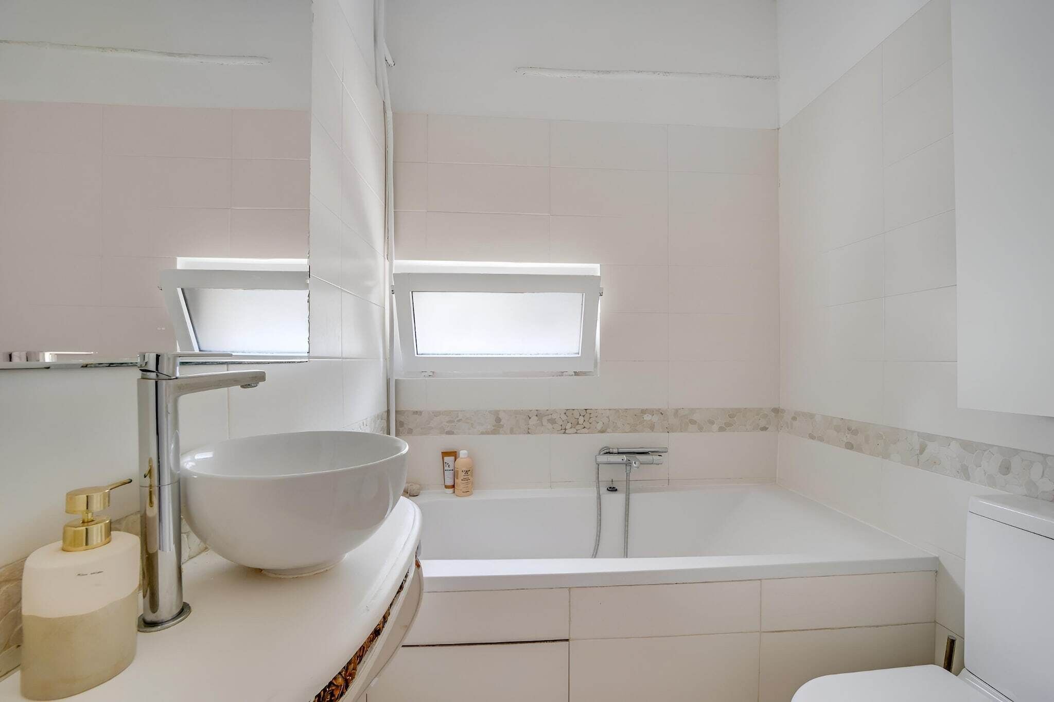 Une salle de bain avec un lavabo blanc, une baignoire et une fenêtre située au-dessus de la baignoire.